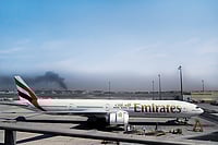 The Gulf Widens: West Asia Faces No-Win Scenario as War On Iran Raises Fears of Instability | Photo: AP : Enveloped by Darkness: A plume of smoke caused by an Iranian strike is seen in the background of an Emirates plane parked at the Dubai International Airport on March 1, 2026