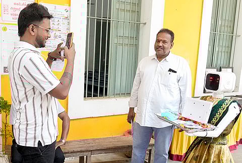 People take photographs with a robot wearing a saree at a polling station during the Puducherry Assembly elections, in Puducherry.
