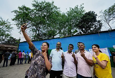 A woman takes photograph of a group with indelible ink mark on their index fingers as people stand in queue to cast their votes at a polling center during the state election in Guwahati.