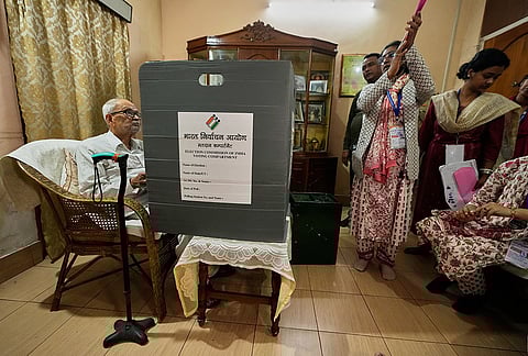 A polling official instructs 96-year-old Jatindra Chandra Nath, left, who prepares to cast his vote ahead of state assembly election using a postal ballot behind a portable screen at his residence in Guwahati, India, Tuesday, March 31, 2026. 