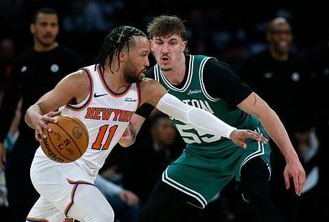 New York Knicks guard Jalen Brunson, left, dribbles around Boston Celtics guard Baylor Scheierman, right, during the second half of an NBA basketball game in New York.