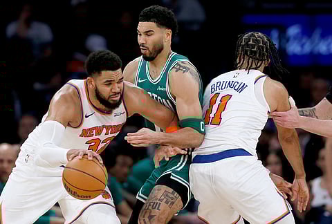 New York Knicks center Karl-Anthony Towns, left, dribbles around Boston Celtics forward Jayson Tatum, center, and Knicks guard Jalen Brunson (11) during the second half of an NBA basketball game in New York. 