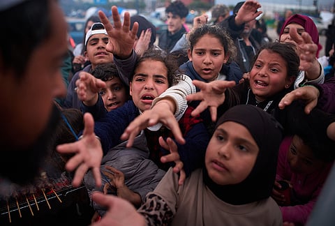Displaced families extend their hands while waiting for donated food beside the tents they use as shelters after fleeing Israeli bombardment in southern Lebanon, in Beirut, Lebanon, Thursday, April 9, 2026. 