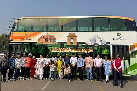Passengers pose with a Delhi Tourism electric double-decker bus, launched for curated sightseeing tours across central Delhi, in New Delhi.