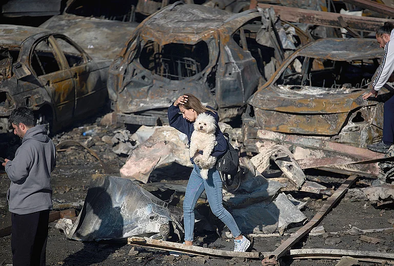 A woman holds her dog as she walks past burned cars a day after an Israeli airstrike in Beirut, Lebanon, Thursday, April 9, 2026. - | Photo: AP/Emilio Morenatti