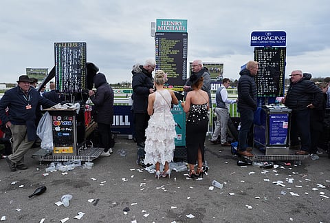 Racegoers stand at a betting booth on Ladies Day, the second day of the Grand National Horse Racing festival, at Aintree racecourse, near Liverpool, England.