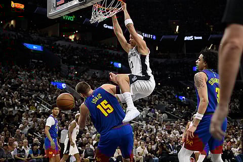 San Antonio Spurs forward Carter Bryant (11) dunks over Denver Nuggets center Nikola Jokic during the first half of an NBA basketball game in San Antonio.