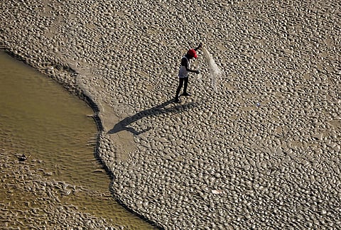A fisherman cleans his net on the exposed riverbed of the Ganga amid receding water levels on a hot summer day, in Prayagraj.