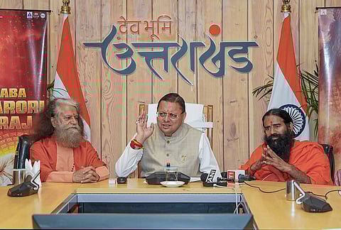 Uttarakhand Chief Minister Pushkar Singh Dhami, centre, speaks to the media about a film based on Neem Karoli Baba as Swami Chidanand Saraswati, left, and Baba Ramdev look on, in Dehradun. 