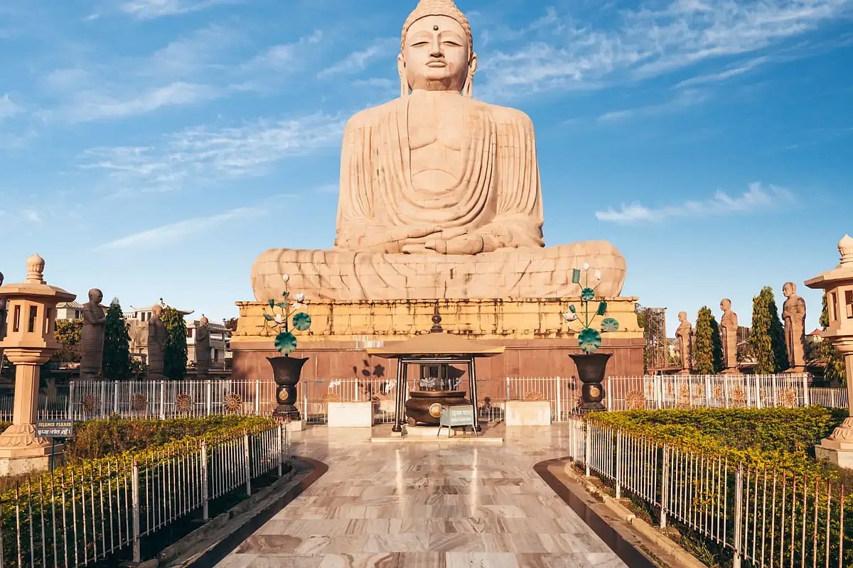 Large seated Buddha statue at a temple with blue sky background and pathway leading up to it