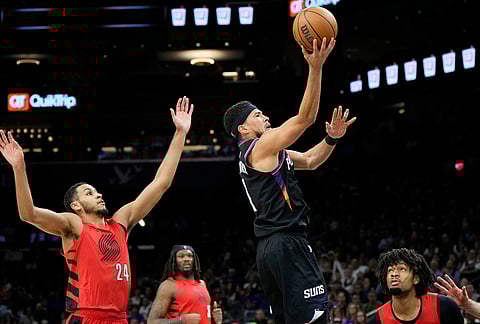 Phoenix Suns guard Devin Booker (1) drives past Portland Trail Blazers forward Kris Murray (24) as Trail Blazers center Robert Williams III and Portland Trail Blazers guard Shaedon Sharpe, right, look on during the second half of an NBA play-in tournament basketball game, in Phoenix. 