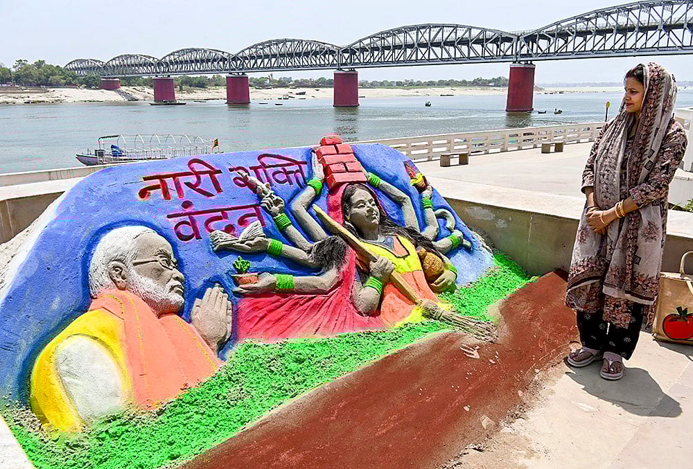 A woman looks at a sand art carved by Sand artist Rupesh Singh dedicated on 'Nari Shakti Vandan Adhiniyam', commonly known as Women's Reservation Act, at Namo Ghat, in Varanasi, Uttar Pradesh. - | Photo: PTI