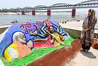 Day In Pics: April 18, 2026 | Photo: PTI : A woman looks at a sand art carved by Sand artist Rupesh Singh dedicated on 'Nari Shakti Vandan Adhiniyam', commonly known as Women's Reservation Act, at Namo Ghat, in Varanasi, Uttar Pradesh.
