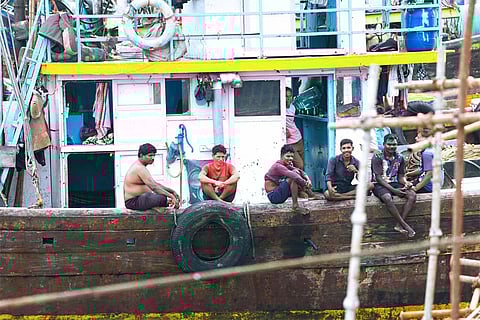 Fishermen wait beside idle crates at Sassoon Dock as activity slows amid market uncertainty.