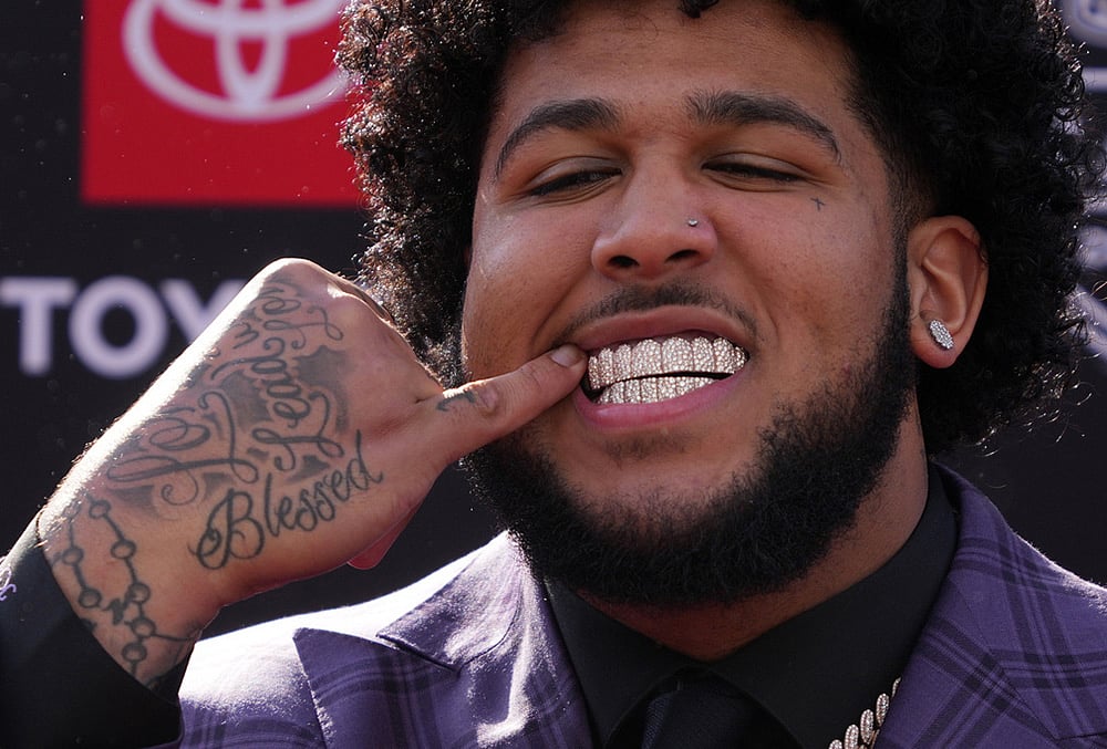 Alabama offensive lineman Kadyn Proctor shows off his dental jewelry while posing on the red carpet before the first round of the NFL football draft in Pittsburgh - | Photo: AP/Gene J. Puskar