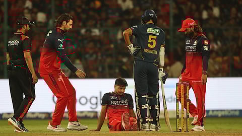 Royal Challengers Bengaluru's Rasikh Dar sits on the ground after getting injured during the Indian Premier League cricket match between Royal Challengers Bengaluru and Gujarat Titans in Bengaluru, India, Friday, April 24, 2026.