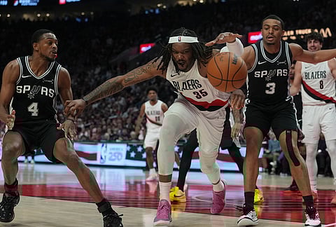 Portland Trail Blazers center Robert Williams III (35) reaches for a loose ball between San Antonio Spurs guard De'aaron Fox (4) and forward Keldon Johnson (3) during the second half in Game 3 of a first-round NBA playoffs basketball series in Portland, Oregon.