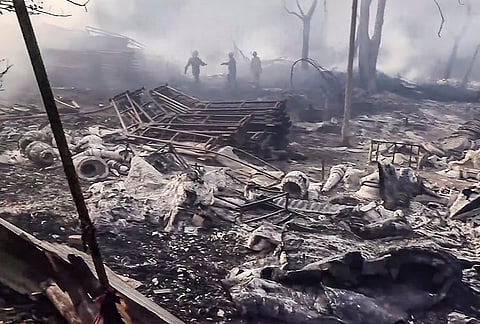 Firemen sift through charred remains while smoke billows after a fire at a tent godown at Jyoti Nagar area, in New Delhi.