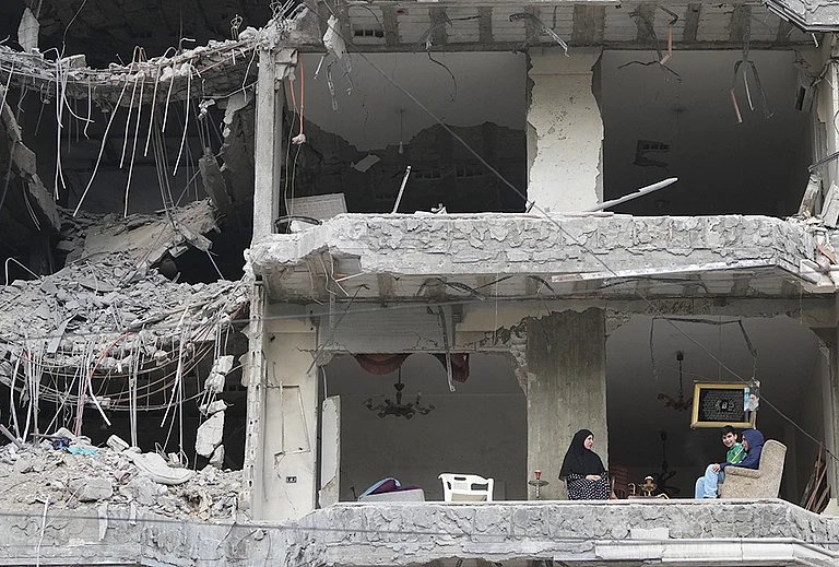 The wife and children of Fadi Al Zein, who lost both his homes in Israeli strikes in his village of Khiam and in Dahiyeh, sit on the balcony of their heavily damaged apartment building in Beirut's southern suburbs, Lebanon, Saturday, April 25, 2026. - | Photo: AP/Hassan Ammar