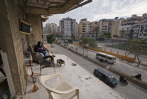 The wife of Fadi Al Zein, who lost both his homes in Israeli strikes in his village of Khiam and in Dahiyeh, sits on the balcony of their damaged home as traffic passes below in Beirut's southern suburbs, Lebanon, Saturday, April 25, 2026. 