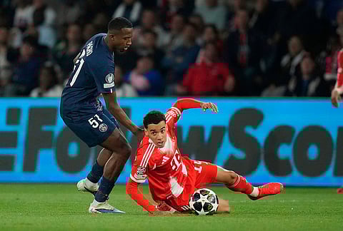 Bayern's Jamal Musiala, bottom, and PSG's Willian Pacho challenge for the ball during the Champions League semifinal first leg soccer match between Paris Saint-Germain and Bayern Munich in Paris.
