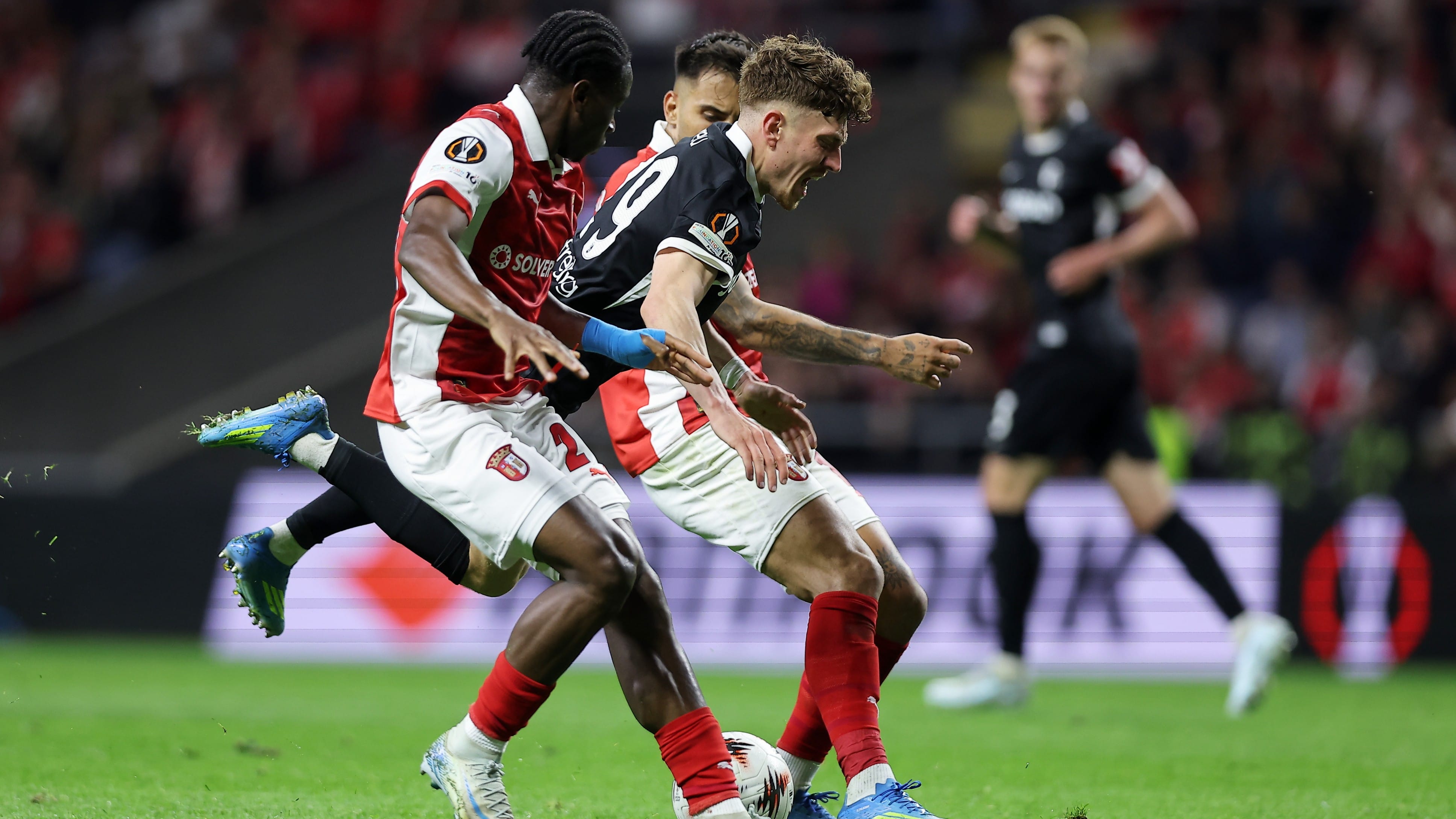 Freiburg's Philipp Treu falls down between Braga's Mario Dorgeles, left, and Rodrigo Zalazar during the Europa League semifinal, first leg, soccer match between SC Braga and Freiburg in Braga, Portugal, Thursday, April 30, 2026. - | Photo: AP/Miguel Angelo Pereira