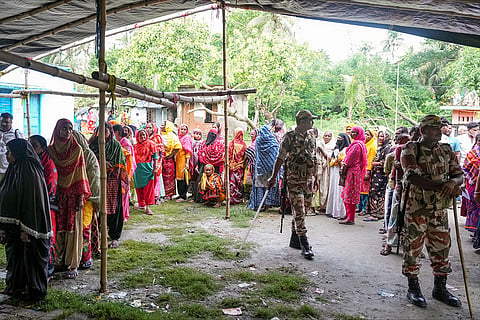 Security personnel stand guard as voters wait in a queue to cast their votes during a repoll for the West Bengal Assembly elections, ordered by the Election Commission following reports of electoral malpractices, at Magrahat Paschim constituency, in South 24 Parganas district.