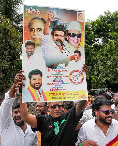 A supporter holds a portrait of Tamilaga Vettri Kazhagam (TVK) chief Vijay during vote tabulation on the day of Assembly election results, near party headquarters in Chennai.