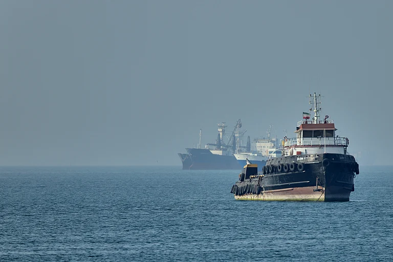 An Iranian tugboat floats in the foreground as cargo ships sit at anchor in the Strait of Hormuz off Bandar Abbas, Iran. - PTI