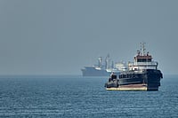 India Denounces Fujairah Strike; Demands Urgent End to Regional Violence PTI : An Iranian tugboat floats in the foreground as cargo ships sit at anchor in the Strait of Hormuz off Bandar Abbas, Iran.