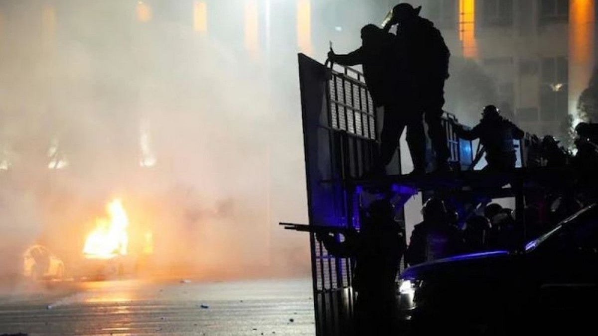 A cop car is set on fire as riot police prepare to stop protesters in the centre of Kazakhstan.