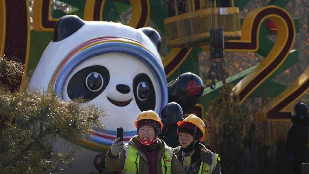 Workers take selfie as others set up a decoration for the Winter Olympic Games 2022.