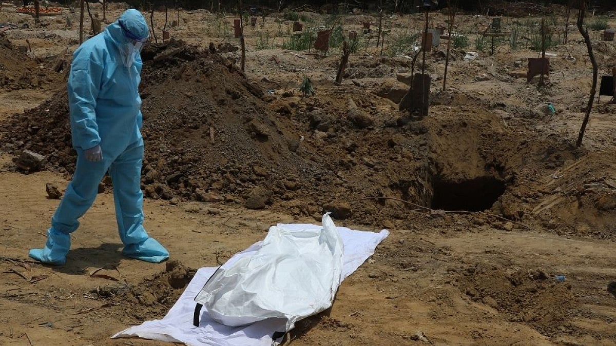 A man wrapped in a PPE kit, starring down at a body. 