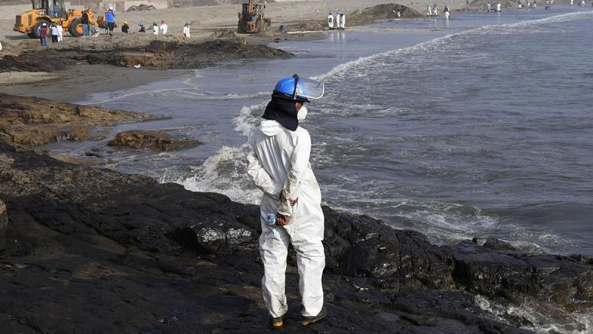 A worker stands on a rock covered with oil in Peru.