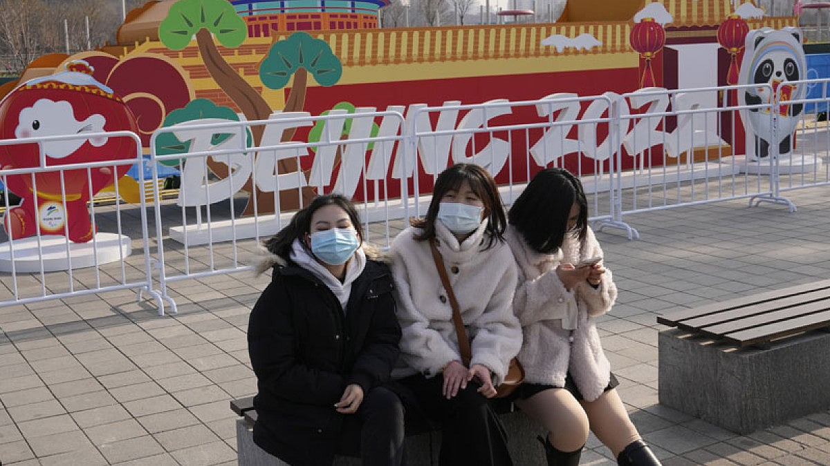 Women wearing masks rest on a bench near Beijing Winter Olympics decorations on the Olympic Green.