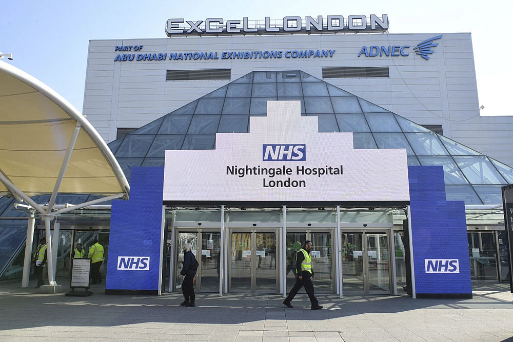 People walk past the ExCel Centre in London, Friday March 27, 2020. The British Government announced Tuesday that the ExCel Center in east London will become a 4,000 bed temporary hospital to deal with future coronavirus patients, to be called NHS Nightingale. The new coronavirus causes mild or moderate symptoms for most people, but for some, especially older adults and people with existing health problems, it can cause more severe illness or death.