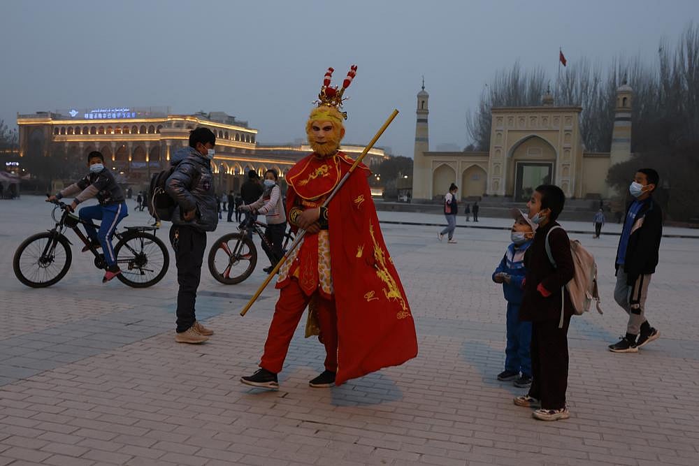 A performer dressed as the monkey god from a Chinese fable walks near a mosque as Uyghur children gaze upon him in Xinjiang.
