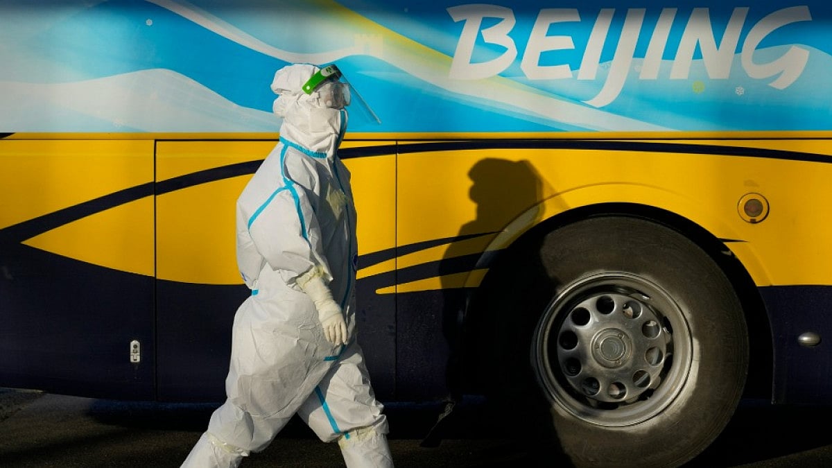 A worker wearing a protective suit walks beside a bus at the 2022 Winter Olympics.