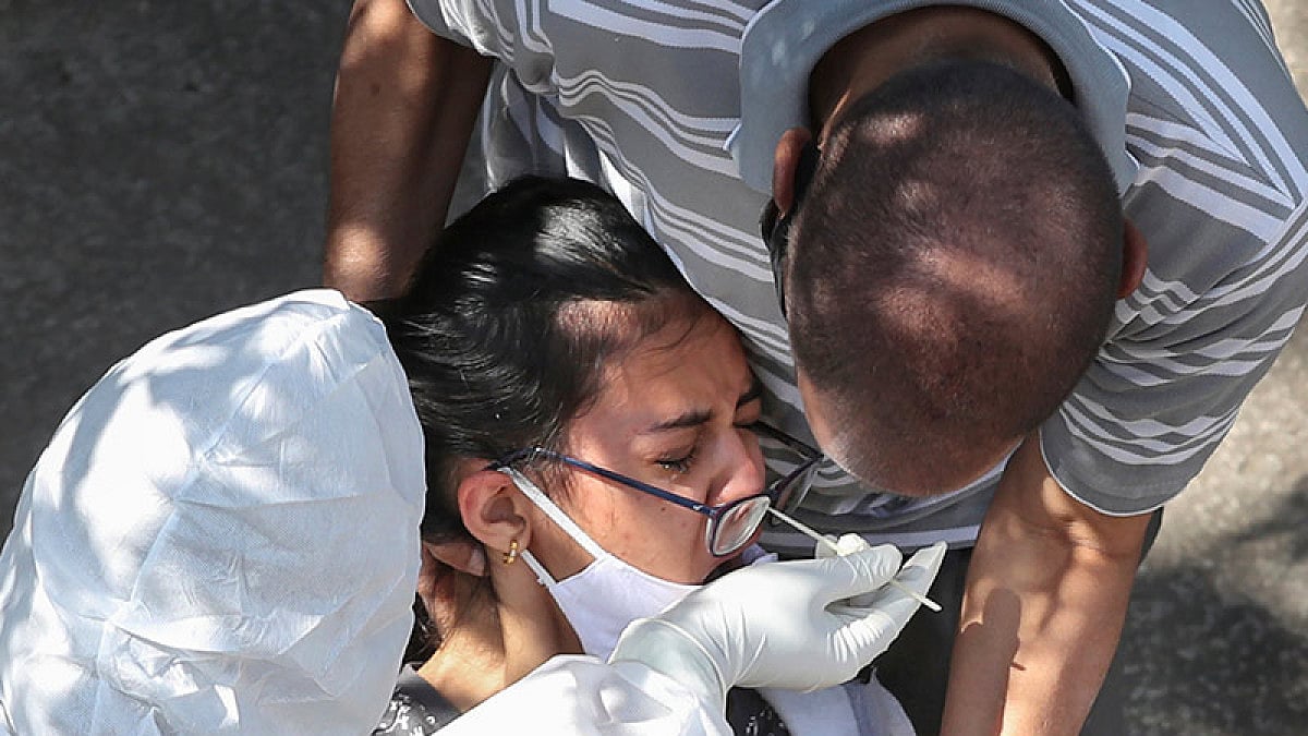 A father holds her daughter while a health worker takes a swab sample to test for COVID-19.