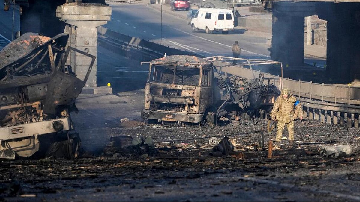 A Ukrainian soldier walks past debris of a burning military truck, on a street in Kyiv, Ukraine.