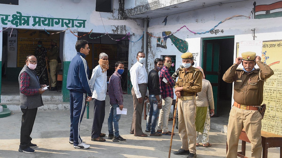 Security personnel stand guard as people wait to cast their vote in Prayagraj