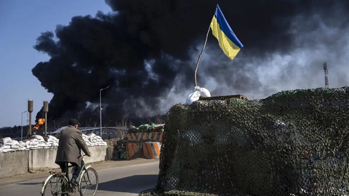A man rides a bicycle as black smoke rises from a fuel storage on the outskirts of Kyiv, Ukraine.