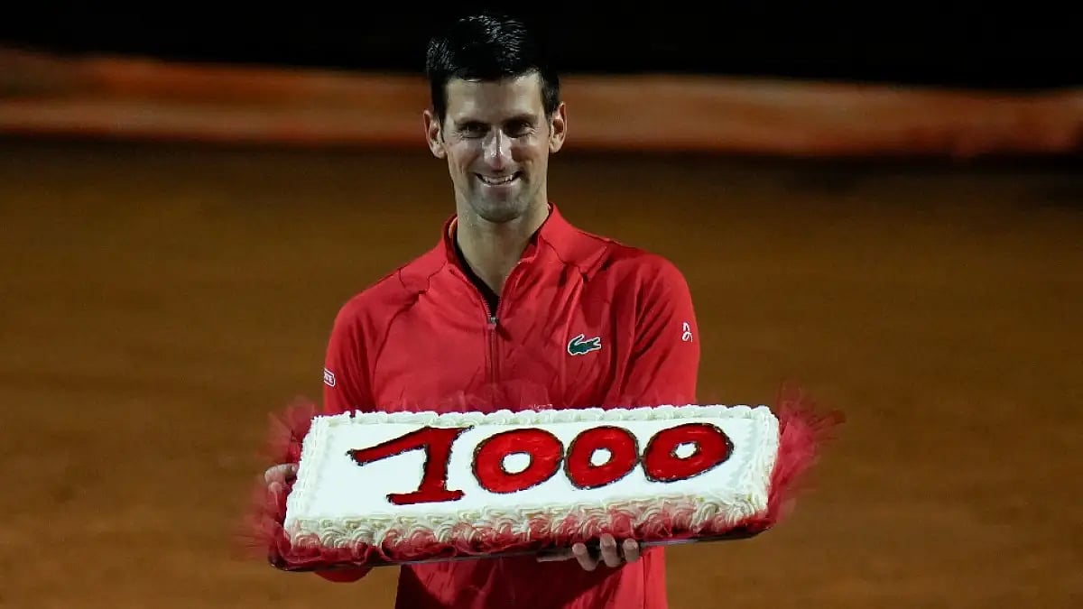 Novak Djokovic holds a cake adorned with the number of his 1,000th tour-level wins.