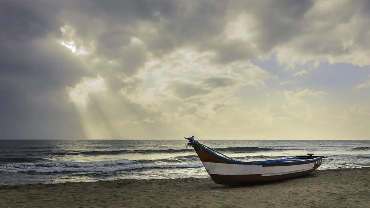 A fishing boat stands moored on a sandy beach at dawn during the monsoon in Mamallapuram
