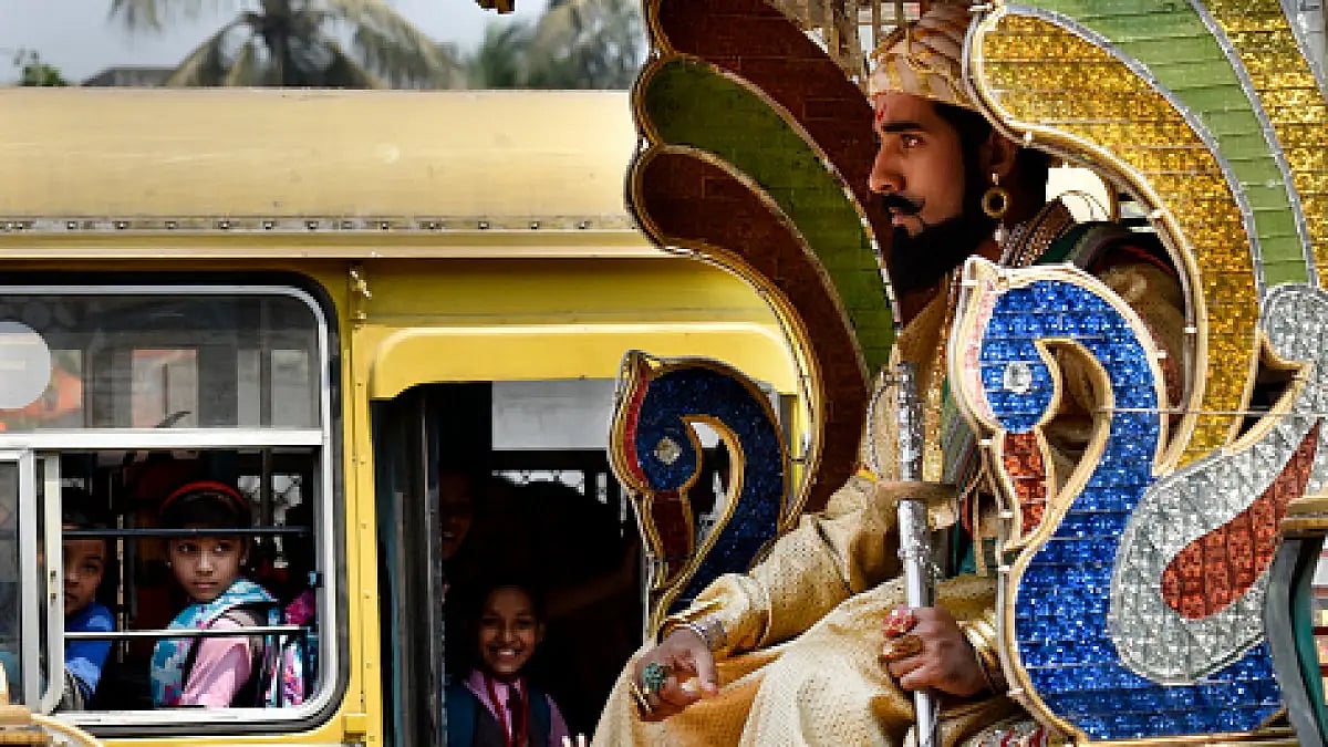 Schools kids watching as a man dressed like Chatrapati Shivaji Maharaj rides a horse pulled chariot 