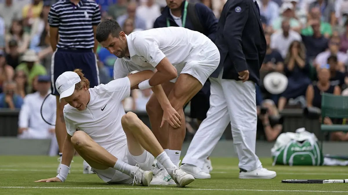 Novak Djokovic helps Jannik Sinner to his feet after he slipped during their singles quarterfinal match at Wimbledon 2022.