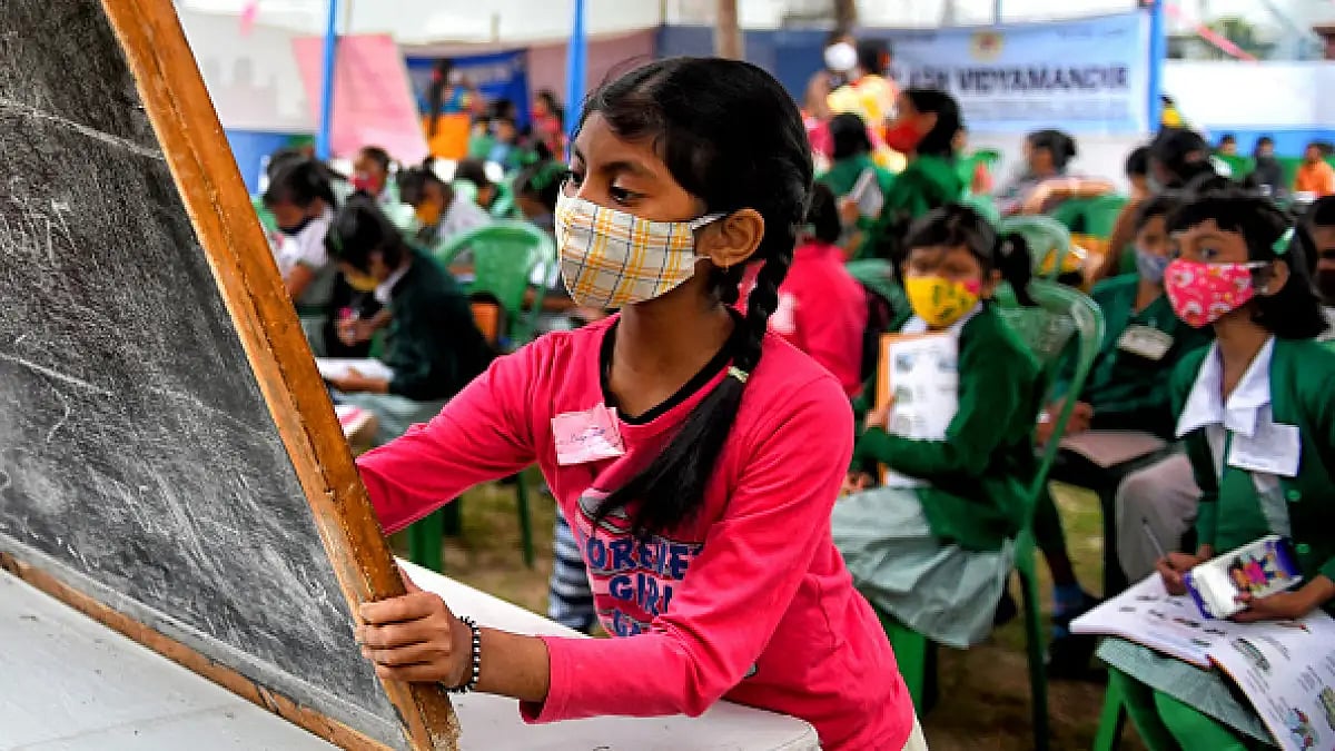 A young girl seen writing on a chalkboard as she attends a class in the open air.