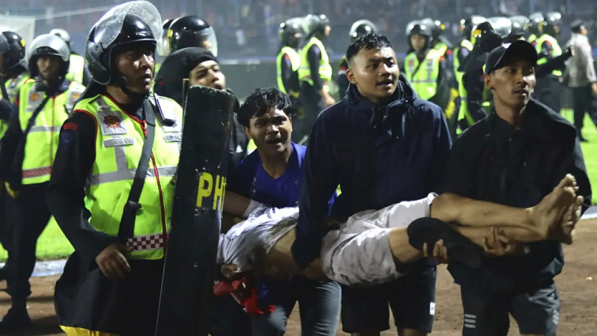 Fans carry an injured man following clashes during a football match at Kanjuruhan Stadium.