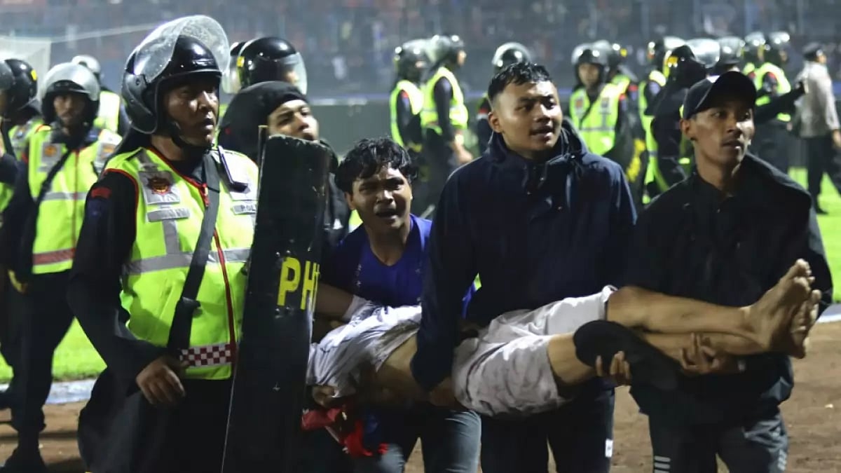 Football fans carry an injured man following clashes during the Arema FC vs Persebaya Surabaya tie.