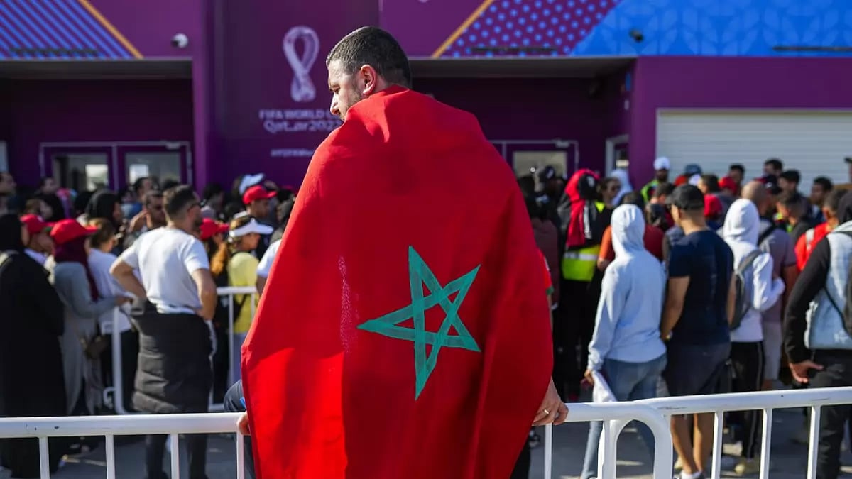 A man draped in a Moroccan flag stands with fans outside the Al Janoub Stadium in Wakrah.